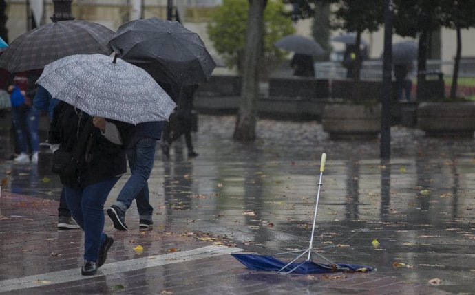 Personas se protegen de la lluvia durante la borrasca 'Elsa', a la que la Confederación Hidrográfica del Gualdalquivir ha apuntado como factor de incremento de la capacidad de embalse.