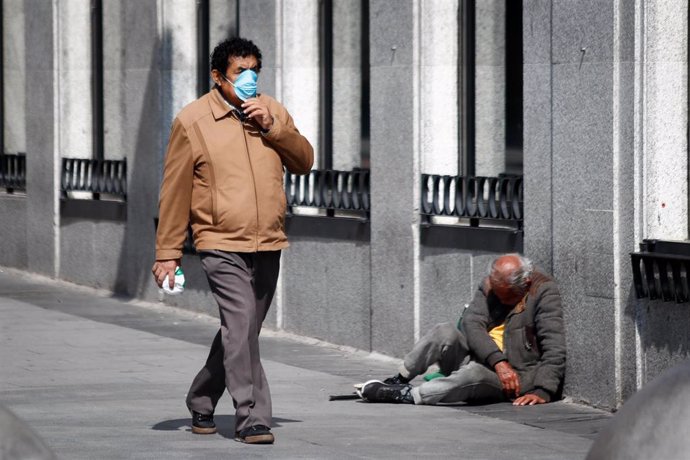 Un hombre con mascarilla pasa junto a una persona sin hogar durante la crisis del coronavirus, en Madrid, a 15 de marzo de 2020.