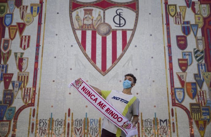 Un hombre posa con una bufanda del equipo ante el escudo del Sevilla FC   