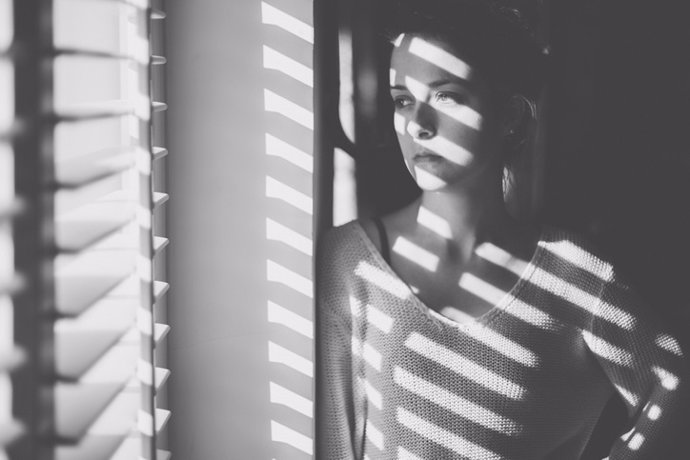 Mujer con deprensión frente a la ventana en su casa. Confinamiento, salud mental. Covid-19