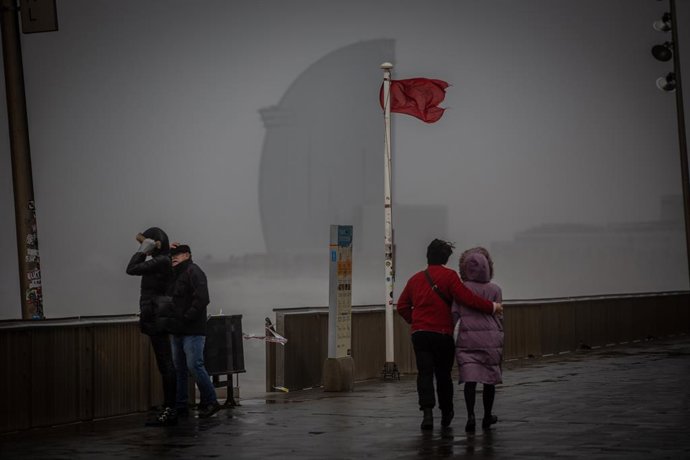 Diverses persones passegen  al costat de la bandera vermella de la platja a Barcelona. Foto d'arxiu.