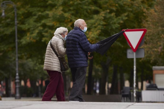 Una pareja de personas mayores, protegidas con mascarillas, pasea por la calle de una ciudad.