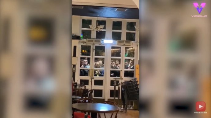Aficionados escoceses terminan de ver un partido de fútbol a través del cristal del bar que acaba de desalojarlos