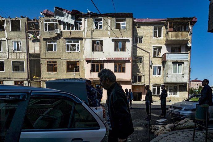 FILED - 03 October 2020, Azerbaijan, Stepanakert: People stand in front of a destroyed building after the impact of a rocket into it during the fighting between Armenia and Azerbaijan over the the breakaway region of Nagorno-Karabakh, also known as Arts