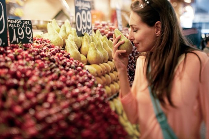 Woman Smelling at Pear at Fruit Stand