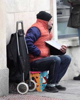 Un mendigo con ropa de abrigo y sentado en una caja, pide dinero en la calle