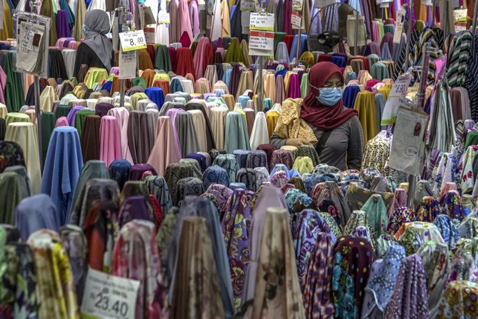 01 June 2020, Malaysia, Luala Lumpur: A woman wearing a face mask walks walks through stands of textile at a store after restrictions imposed on markets have been partially lifted after staying in effect for several weeks amid the coronavirus pandemic. 
