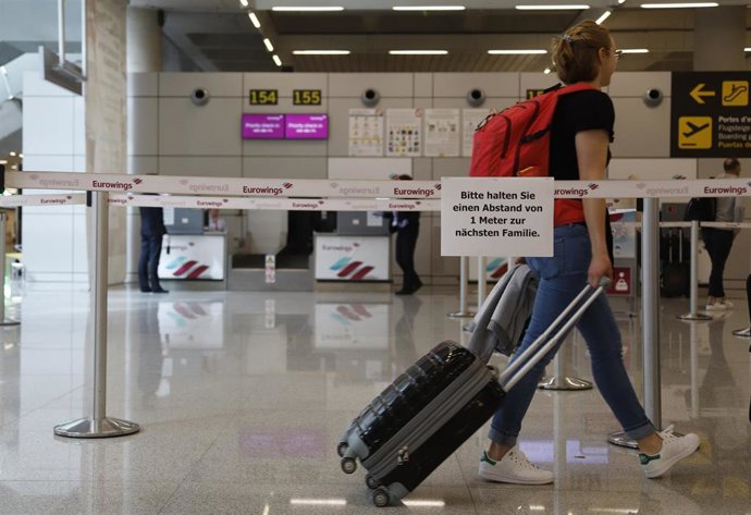 Un viajero en el aeropuerto de Palma, pasando con su equipaje junto a un cartel informativo en alemán.