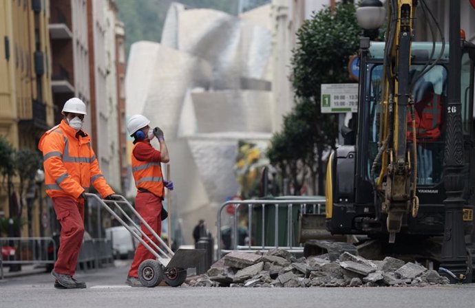 Dos operarios trabajan en la obra de una calle cerca del Museo Guggenheim durante su jornada laboral el día en el que se reactiva la actividad laboral no esencial,, en Bilbao (País Vasco, España), a 14 de abril de 2020.