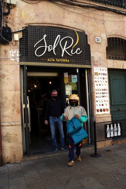 Pla general d'un repartidor a domicili recollint la comanda d'un restaurant que ha obert a la plaa de la Font en el primer dia de restriccions. Imatge del 16 d'octubre del 2020 (Vertical):