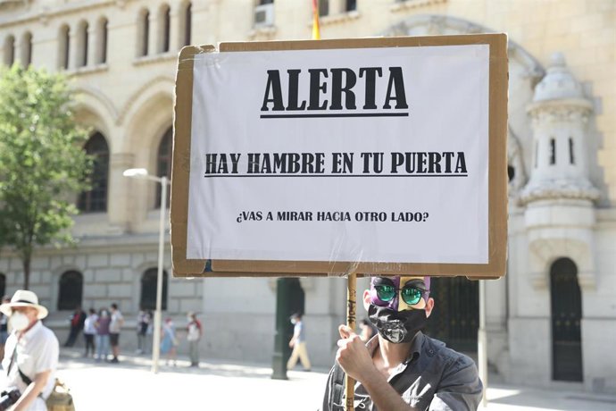 Un joven sostiene una pancarta donde se puede leer "Alerta, hay hambre en tu puerta" durante una manifestación de las entidades ciudadanas que están dando respuesta a las 'colas del hambre' ante el Palacio de Cibeles, sede del Ayuntamiento de Madrid (Es