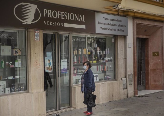 Una mujer en la puerta de una tienda de artículos de peluquería. En Sevilla, (Andalucía, España) a 30 de abril de 2020.
