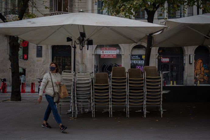 Una dona passa pel costat de la terrassa d'un bar tancat durant el quart dia de l'entrada en vigor de les noves restriccions. Barcelona, Catalunya (Espanya), 20 d'octubre de 2020.