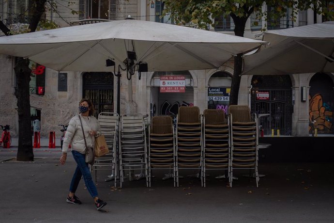 Una mujer pasa junto a la terraza recogida de un bar cerrado durante el cuarto día de la entrada en vigor de las nuevas restricciones en Cataluña, en Barcelona, Cataluña (España) a 20 de octubre de 2020. El pasado viernes 16 de octubre entraron en vigor
