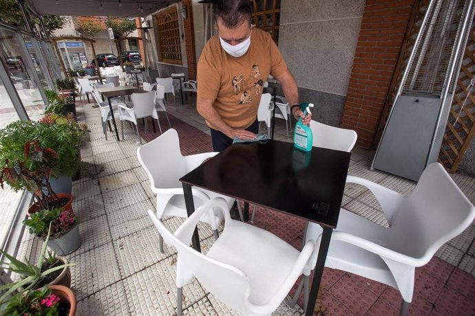 Un camarero limpia una de las mesas de su bar