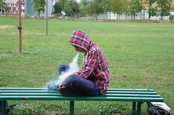 Un joven vapea en el banco de un parque