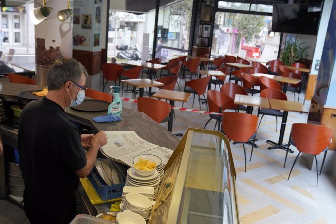 Un camarero lee un periódico en el interior de su bar
