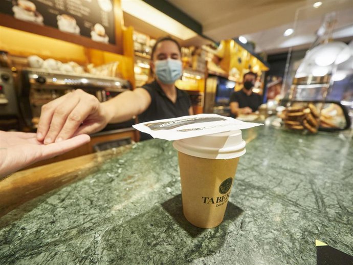 Una camarera de la Cafetería Taberna de Pamplona devuelve el cambio a un cliente tras preparar un café para llevar el día en el que han entrado en vigor las nuevas restricciones en Navarra para tratar de reducir los casos de Covid-19, en Pamplona.