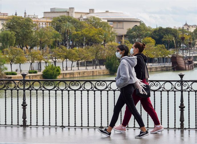 Dos jovenes con mascarillas paseando andando por el puente de Triana en el tercer día de alarma. Sevilla a 17 de marzo 2020