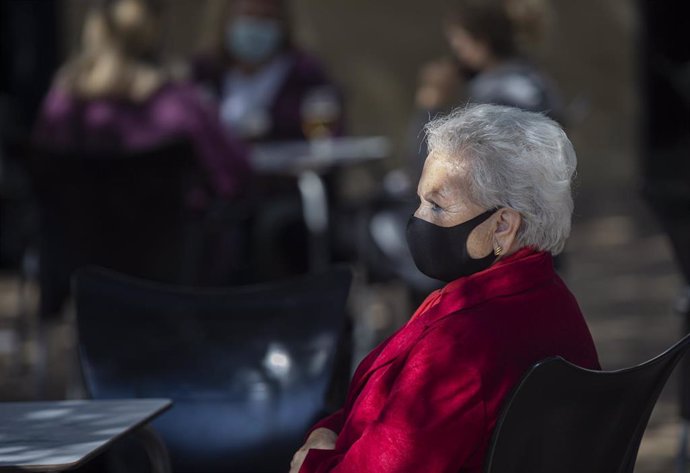 Una mujer mayor con mascarilla en la terraza de un bar