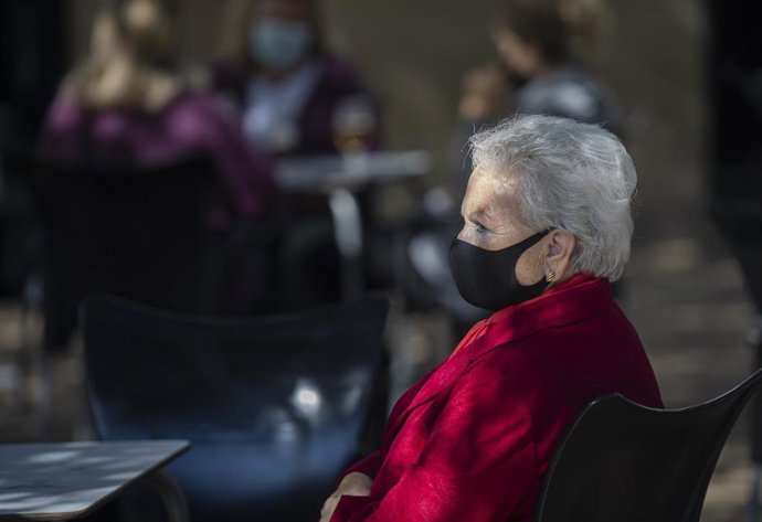 Una mujer mayor con mascarilla en la terraza de un bar.