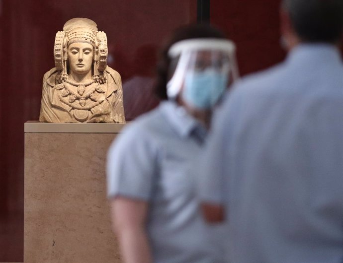 Dos treballadors protegits amb mascarilla i pantalla vigilen una de les sales on es troba l'escultura de la Dama d'Elx