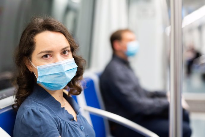 Brunette in medical mask in subway car  Young brunette in medical face mask and protective gloves riding in modern subway car. Concept of forced city trip in context of coronavirus pandemic