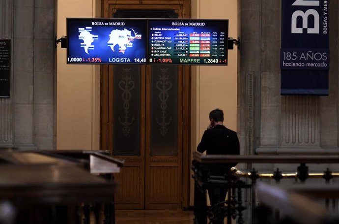 Una persona camina bajo los televisores indicativos con los valores del Ibex en el Palacio de la Bolsa de Madrid (España), a 2 de octubre de 2020. 