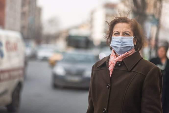 Mujer mayor con mascarilla en una calle con contaminación.