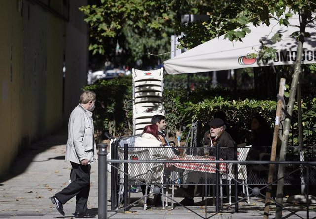 Un hombre camina frente a la terraza de un bar donde hay sentadas otras tres personas en la zona básica de salud de Guzmán el Bueno, en el distrito de Chamberí, en Madrid (España), a 26 de octubre de 2020.