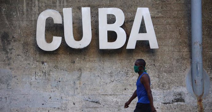 30 April 2020, Cuba, Havana: A man wearing a face mask walks past a sign reading