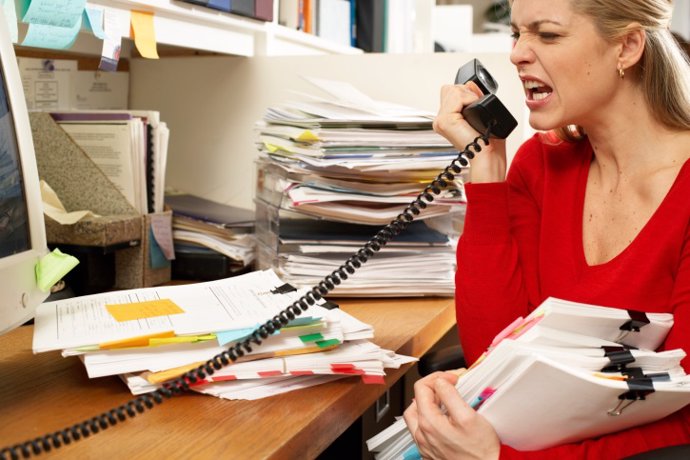 Female office worker holding paperwork, snarling at phone handset
