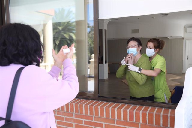 Una residente se comunica con un familiar por una ventana de una residencia.