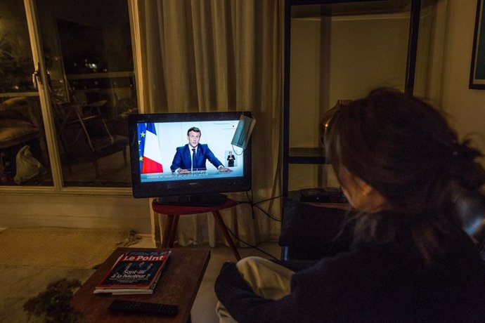 Una mujer sigue el discurso de Emmanuel Macron en su vivienda