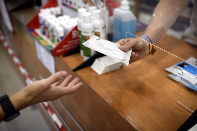 Un farmacéutico entrega a un cliente una de las mascarillas KN95 que ha recibido en su farmacia, en Madrid (España), a 30 de septiembre de 2020.