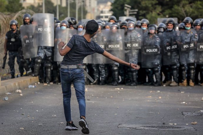 30 October 2020, Lebanon, Beirut: A protester throws stone at riot police protecting the residence of the French ambassador in Beirut, during a demonstration against French President Emmanuel Macron's comments on Islam's prophet Muhammad cartoons. Photo