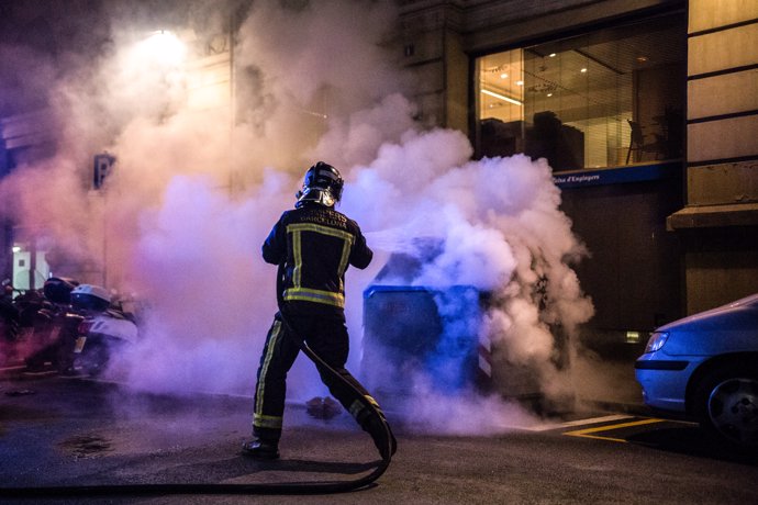 Un bombero apaga un fuego en un cubo de basura quemado por manifestantes durante una protesta por las restricciones por el COVID-19