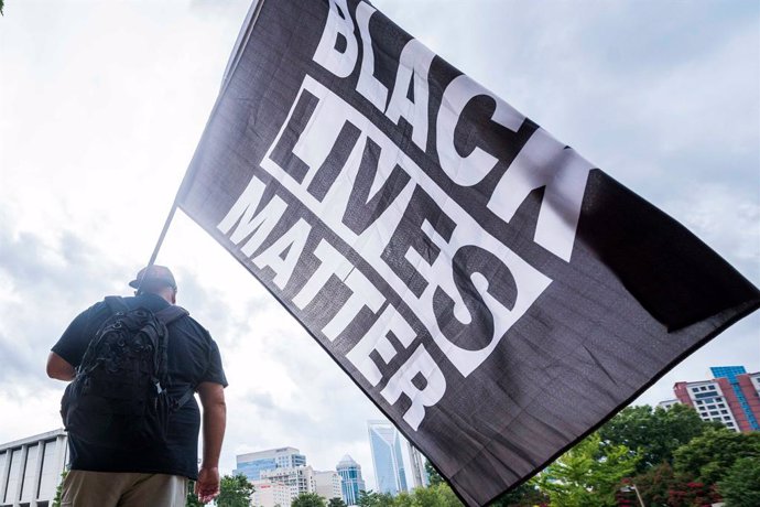 24 August 2020, US, Charlotte: A Black Lives Matter supporter waves a flag during a protest on the opening day of the Republican National Convention. Photo: Sean Meyers/ZUMA Wire/dpa