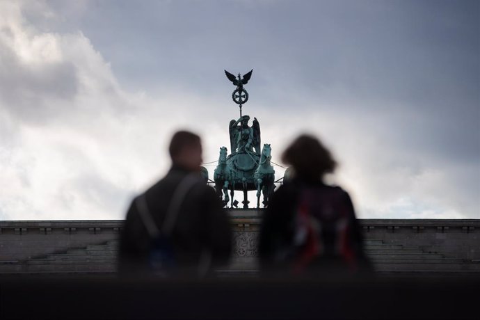 24 October 2020, Berlin: Two passers-by stand in front of the Brandenburg Gate. Photo: Christoph Soeder/dpa