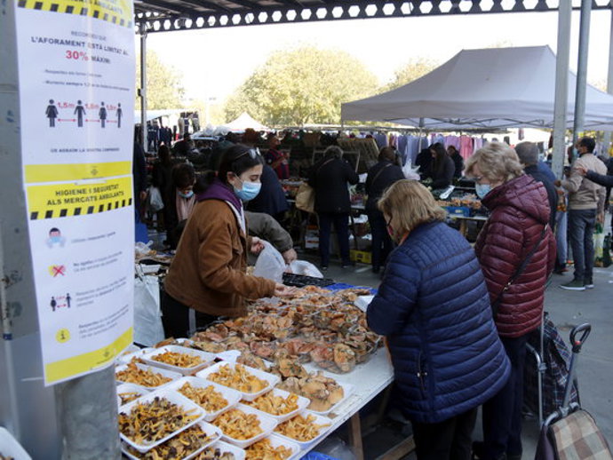 Pla obert de dos cartells al mercat de Barris Nord de Lleida amb les mesures de seguretat que s'han de seguir al recinte, i al fons hi ha dos clients comprant bolets, el 31 d'octubre de 2020. (Horitzontal)