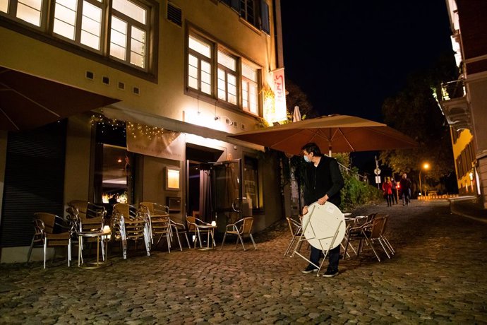 30 October 2020, Baden-Wuerttemberg, Freiburg im Breisgau: A worker of a cocktail bar carries a table in the outdoor area of his bar before closing time. Germany's federal and state governments agreed on last Wednesday to sweeping contact restrictions a
