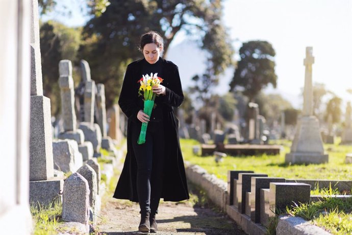 Mujer llevando flores a una tumba en un cementerio.