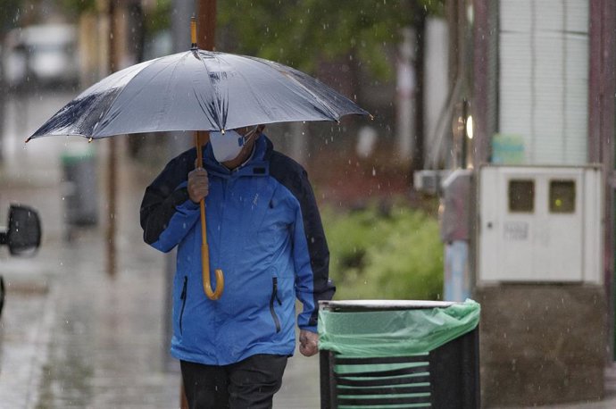Transeúnte protegido con mascarilla y un paraguas 