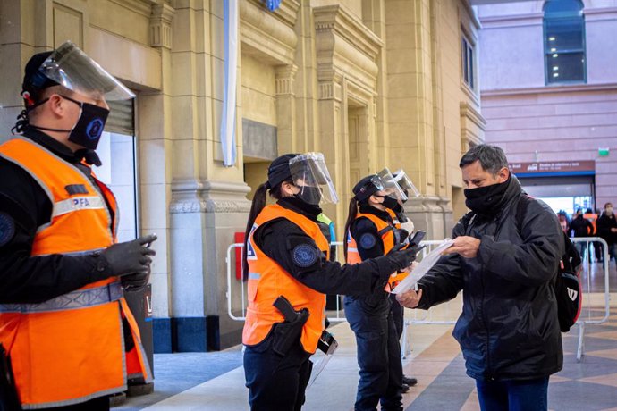 01 July 2020, Argentina, Buenos Aires: Police officers check documents of a passenger at the Constitucion railway station.  Argentina extends and toughens the quarantine in the Buenos Aires metropolitan area from July 1 until July 17 after coronavirus i