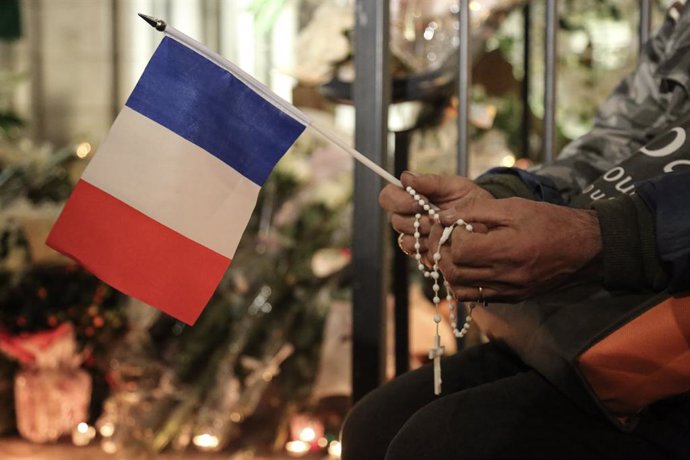 31 October 2020, France, Nice: A person holds the French National flag outside the Notre Dame basilica as people gathered there to pay their respect for the victims of the knife attacking which resulted in killing three people and injuring several other