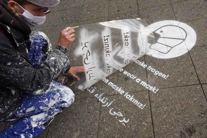 Un hombre pinta un mensaje para recordar la obligación de uso de mascarilla en Berlín