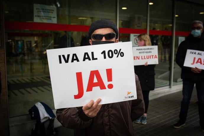 Un hombre sostiene un cartel en el que se lee 'IVA al 10% ja!' durante una concentración frente a la Agencia Tributaria para exigir la bajada del IVA al 10% en el sector de peluquería e imagen personal, en Barcelona, Catalunya (España).
