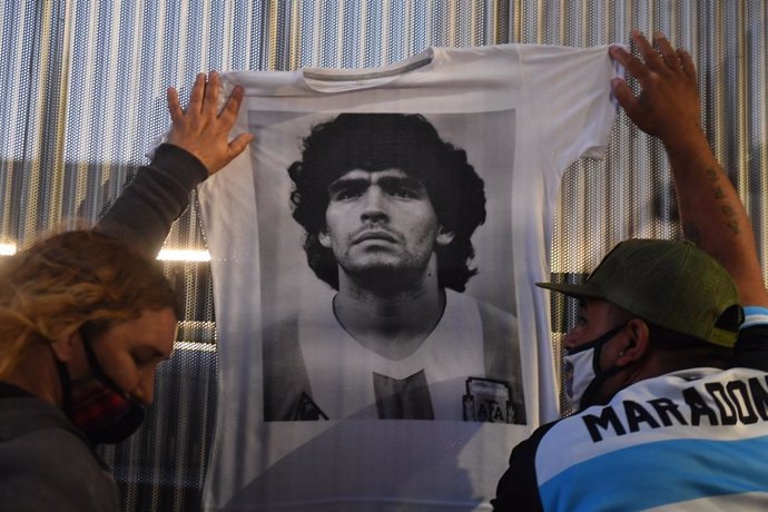 03 November 2020, Argentina, Buenos Aires: Fans of Argentine football legend Diego Maradona hold up a t-shirt with bearing his picture in front of the clinic where Maradona underwent a surgery for a bleed on the brain. Photo: Ramiro Gomez/telam/dpa