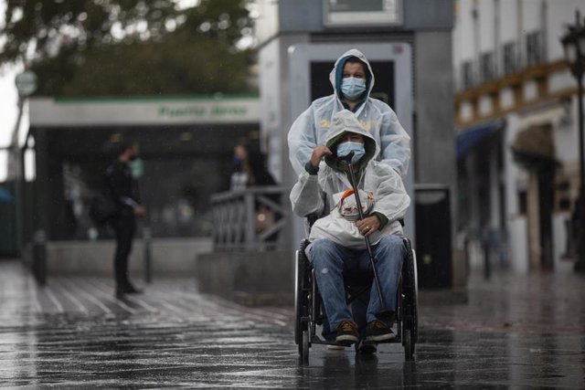 Dos personas con impermeable y mascarillas durante una jornada de lluvia.