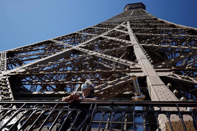 Un hombre con mascarilla asomado a la Torre Eiffel de París, Francia
